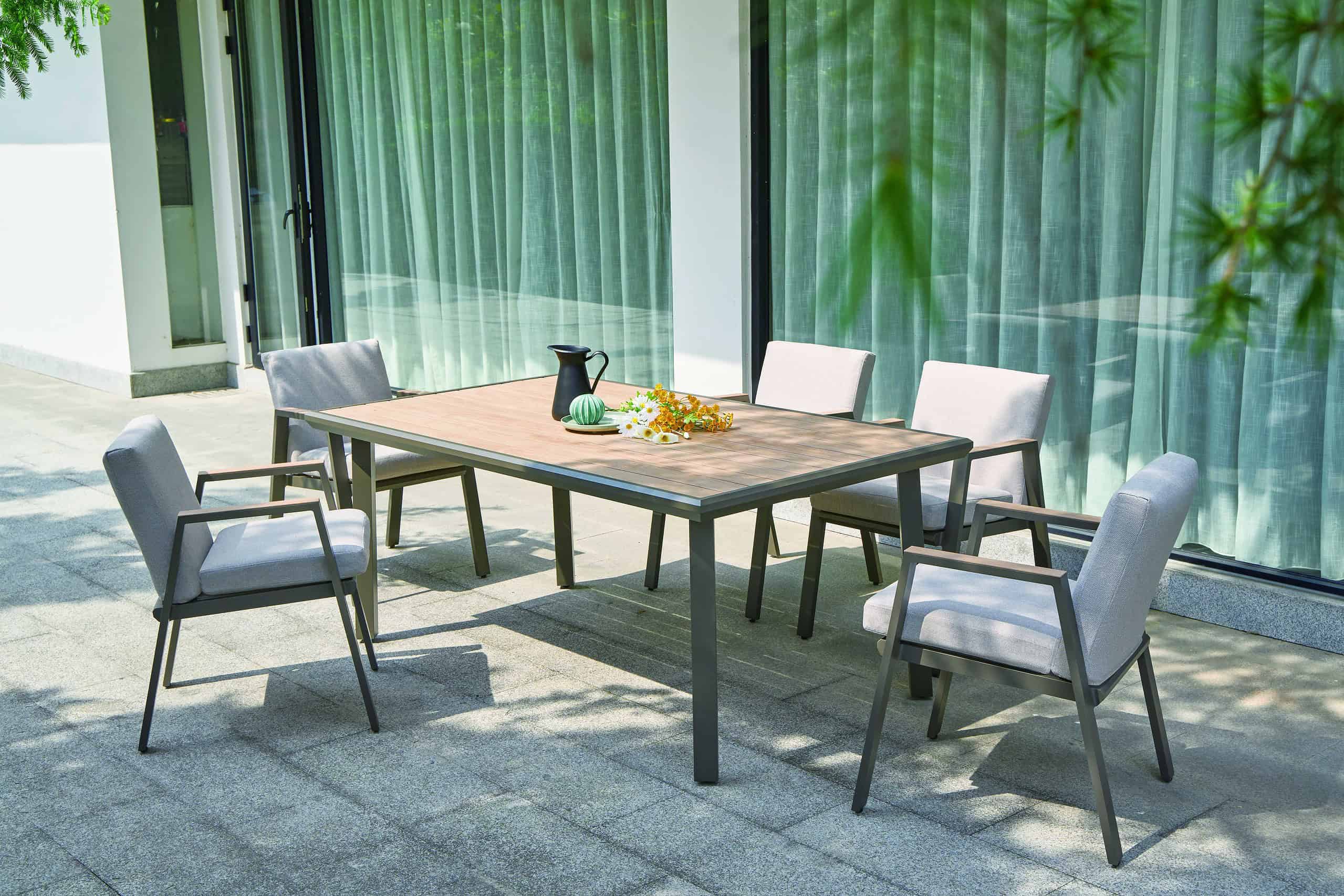 Close-up of a modern grey aluminum garden dining table corner, focusing on textured slats and precise joinery. Natural linen napkins are stacked on the table, with softly blurred autumn leaves and garden path in the background. Soft, diffused daylight highlights textures and muted colors.